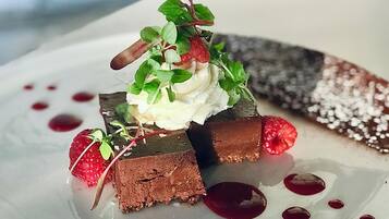 A dessert on a white plate with chocolate pieces, whipped cream, raspberries, and a decorative leaf.