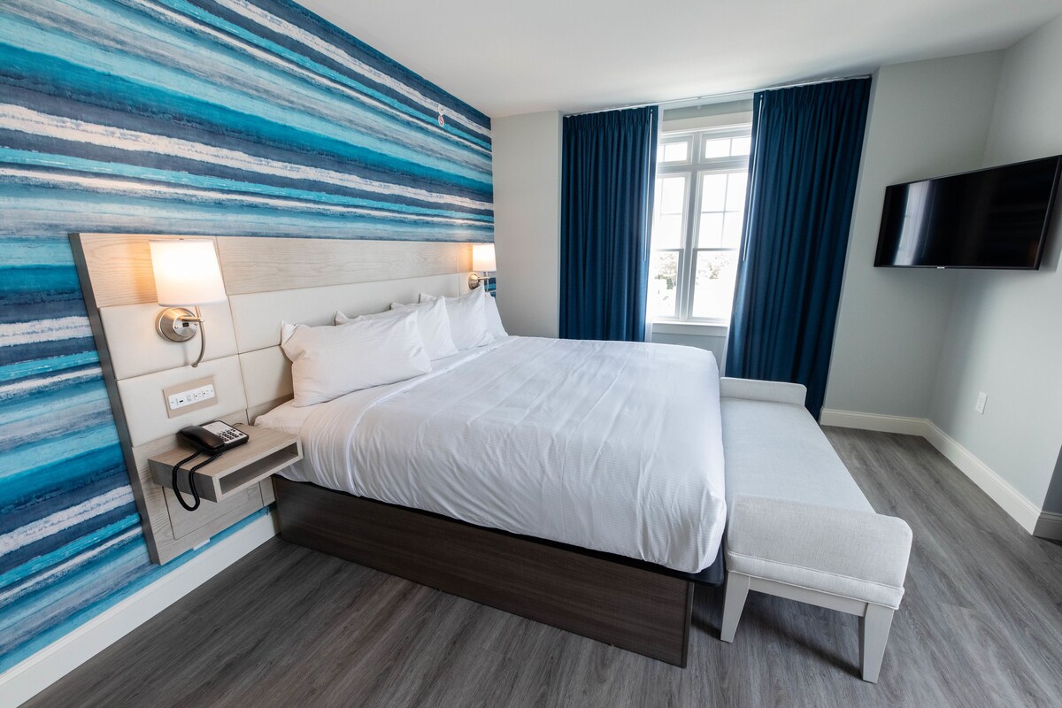 Une chambre d’hôtel moderne dotée d’un grand lit, de lampes de chevet, d’un téléviseur à écran plat et offrant une vue sur l’extérieur.