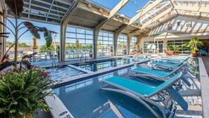 An indoor swimming pool with multiple lanes and lounge chairs, surrounded by large windows and potted plants. - Hotel LBI (Beach Haven)