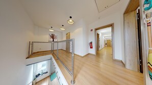 A spacious hallway with wooden flooring, a metal railing, and a fire extinguisher on the wall.