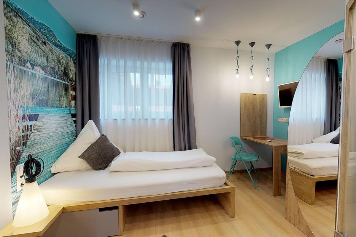 Habitación de hotel moderna con dos camas, un escritorio, una silla, un televisor y un cuadro abstracto grande en la pared.