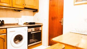 Una cocina compacta con armarios de madera, lavadora, horno y una mesa de madera.