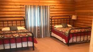 Una habitación de cabaña acogedora con dos camas, paredes de madera, una ventana con cortinas y una mesita pequeña.