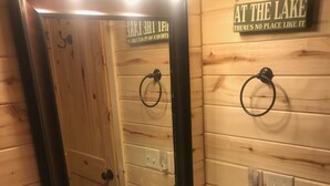 Un baño con pared de madera, un lavabo con espejo y un cartel que dice "EN EL LAGO NO HAY LUGAR COMPARABLE".