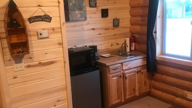 Cocina compacta con paredes de madera, microondas integrado, lavamanos y una ventana pequeña con cortinas.