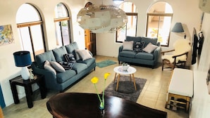 A living room with a dark wooden dining table, two sofas, a coffee table, and a unique ceiling light fixture. - La Buena Vida 2 Amazing (Tamarindo)