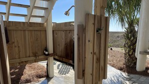 Un espace de douche extérieur en bois, doté d’un sol carrelé, d’une clôture en bois et d’un palmier.