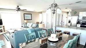 Une cuisine moderne avec des meubles blancs, un îlot central et un coin repas comprenant une table en verre et des chaises de couleur turquoise.
