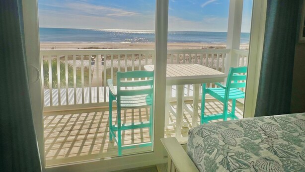Un balcon avec vue sur la plage et l’océan. On y trouve deux chaises et une petite table.