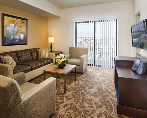 A hotel room with a sofa, armchair, a small table with a vase, a lamp, a TV, and a balcony with blinds. - 1 Bedroom Coachella Weekend Available (Indio)