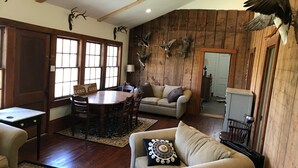 A rustic interior with a wooden ceiling, a dining area with a wooden table and chairs, a beige sofa with decorative pillows, and a wooden wall adorned with animal horns. - Koch Ranch - Hester House  (Columbus)
