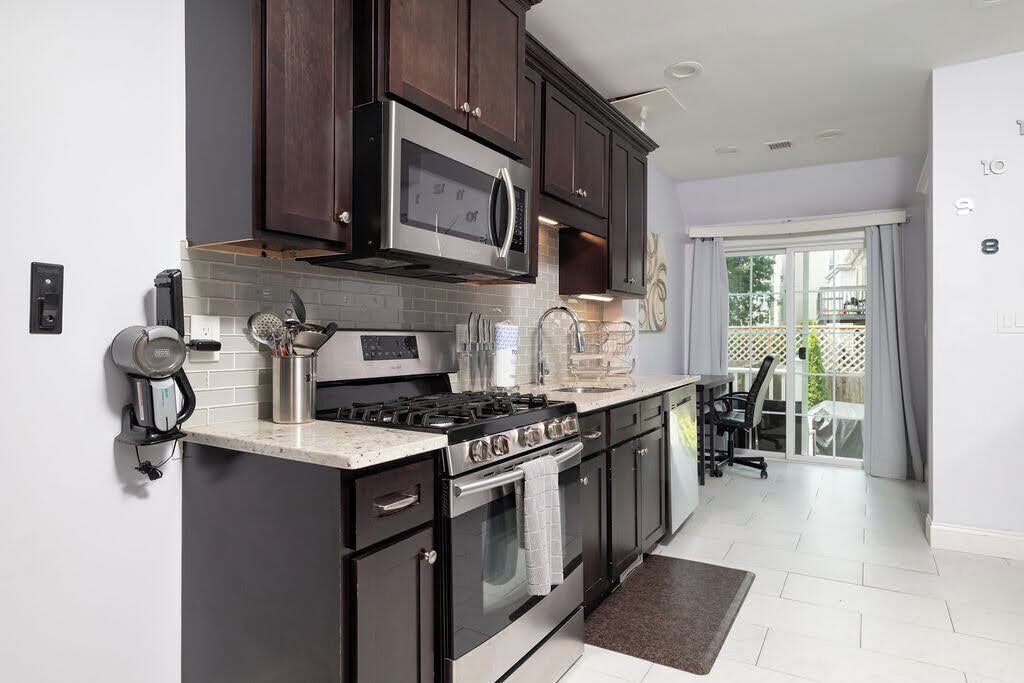 A modern kitchen with dark cabinets, stainless steel appliances, and a large window.