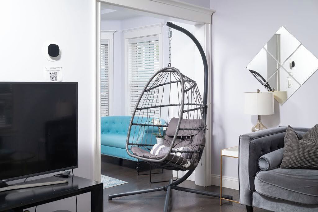 A modern living room with a television, a hanging chair, a sofa, and a mirror on the wall.