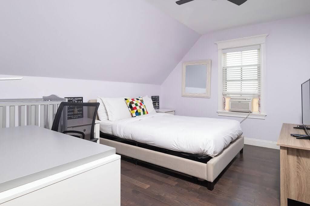 A bedroom with a bed, a desk, a chair, a radiator, and a window with blinds.