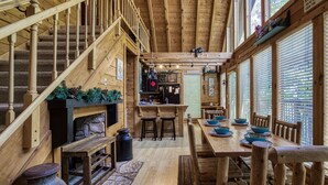 A cabin interior with a wooden staircase, a dining area with blue bowls, and a kitchen area with a stone fireplace. - Mountain Setting Large Screen in Back Porch offers Pool table and Hot Tub Private Setting (Sevierville)