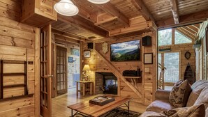 A wooden cabin interior with a fireplace, a television, and a cozy seating area. - Mountain Setting Large Screen in Back Porch offers Pool table and Hot Tub Private Setting (Sevierville)