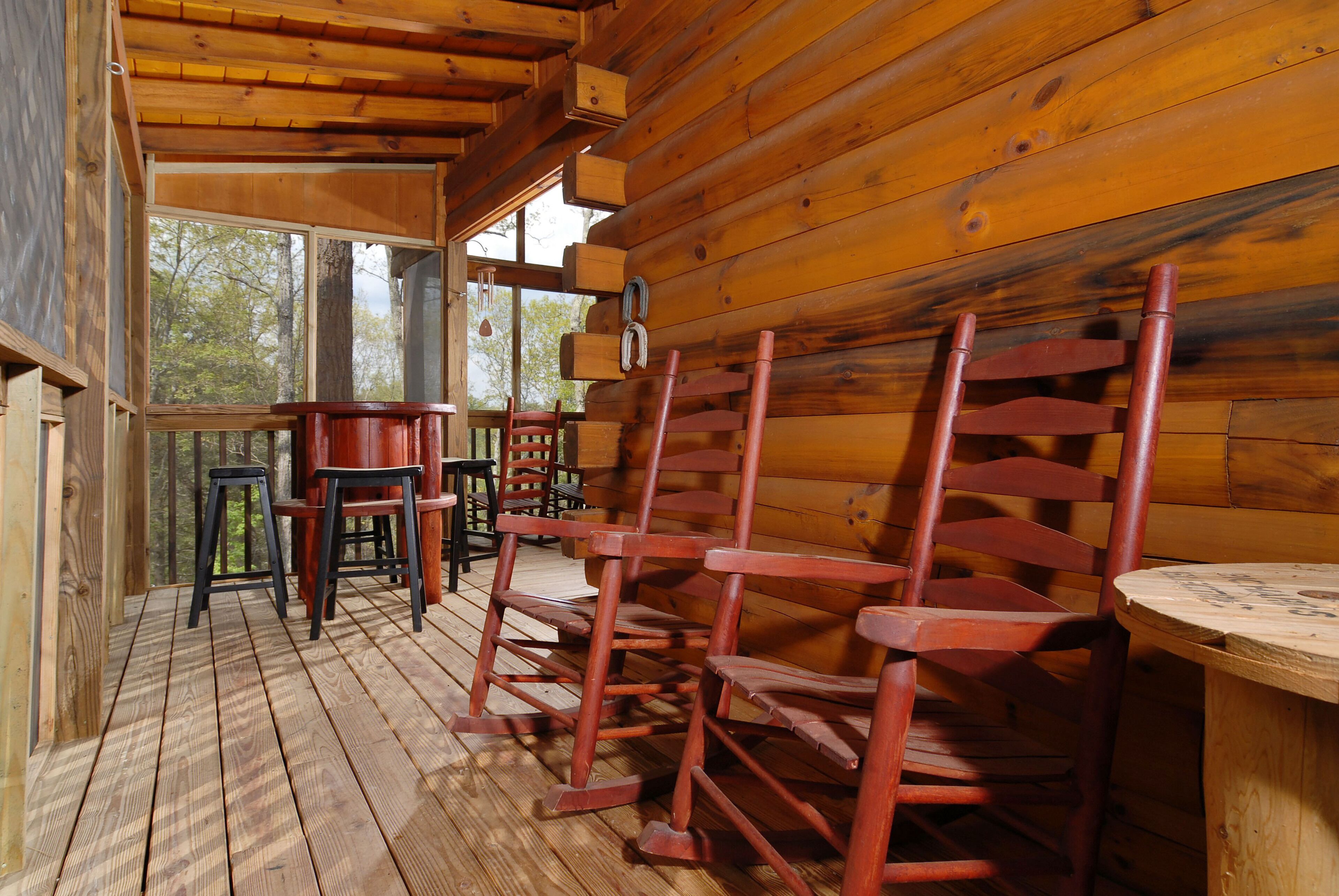 L’intérieur d’un chalet en bois, avec une véranda comprenant plusieurs fauteuils à bascule et une petite table.