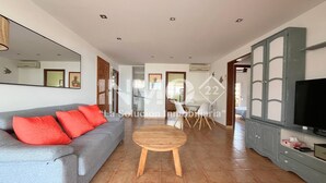 A spacious living room with a grey sofa, red cushions, a wooden coffee table, and a television on a cabinet. - 1st line beach & terrace with sea views (Cambrils)