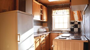 Eine kompakte Küche mit Holzschränken, einem Bosch-Kühlschrank, einem Toaster und einem Fenster mit gemustertem Vorhang.