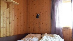 Ein Zimmer mit Holzvertäfelung, einem Bett, einer Wandleuchte und einem Fenster mit Vorhängen.