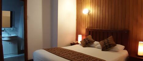 A bedroom with a wooden headboard, a large bed with white bedding, two bedside lamps, and a nightstand.