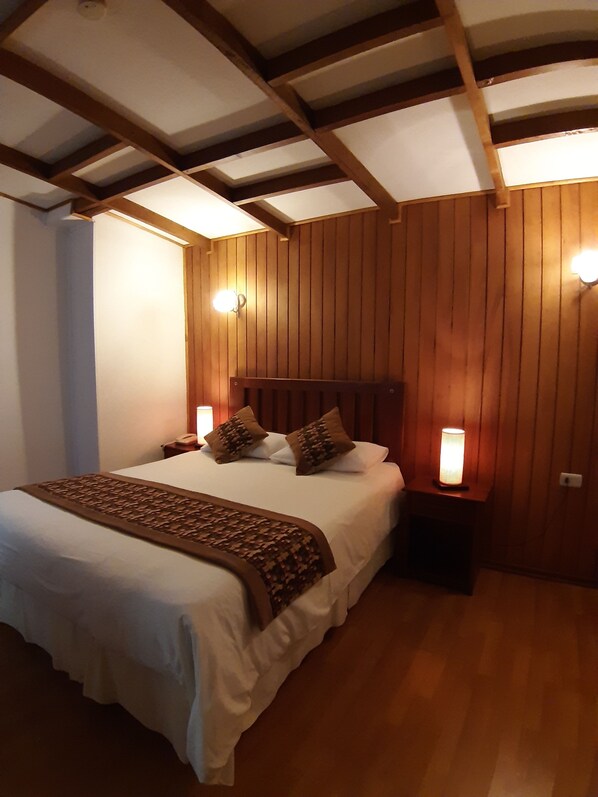 Un dormitorio con cabecera de madera, dos lámparas de noche y una cama con sábanas blancas y almohadas marrones.