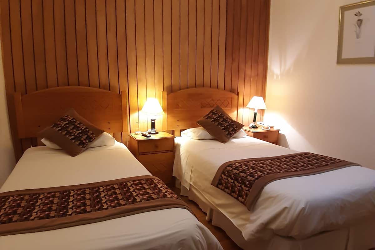 Ein Hotelzimmer mit zwei Betten, Holz-Kopfteilen und Nachttischlampen.