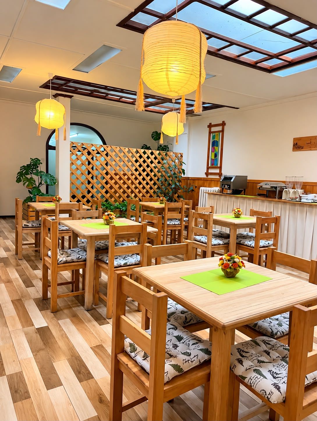 Interior de restaurante com mesas e cadeiras de madeira, divisória de madeira e vista através de um claraboia.