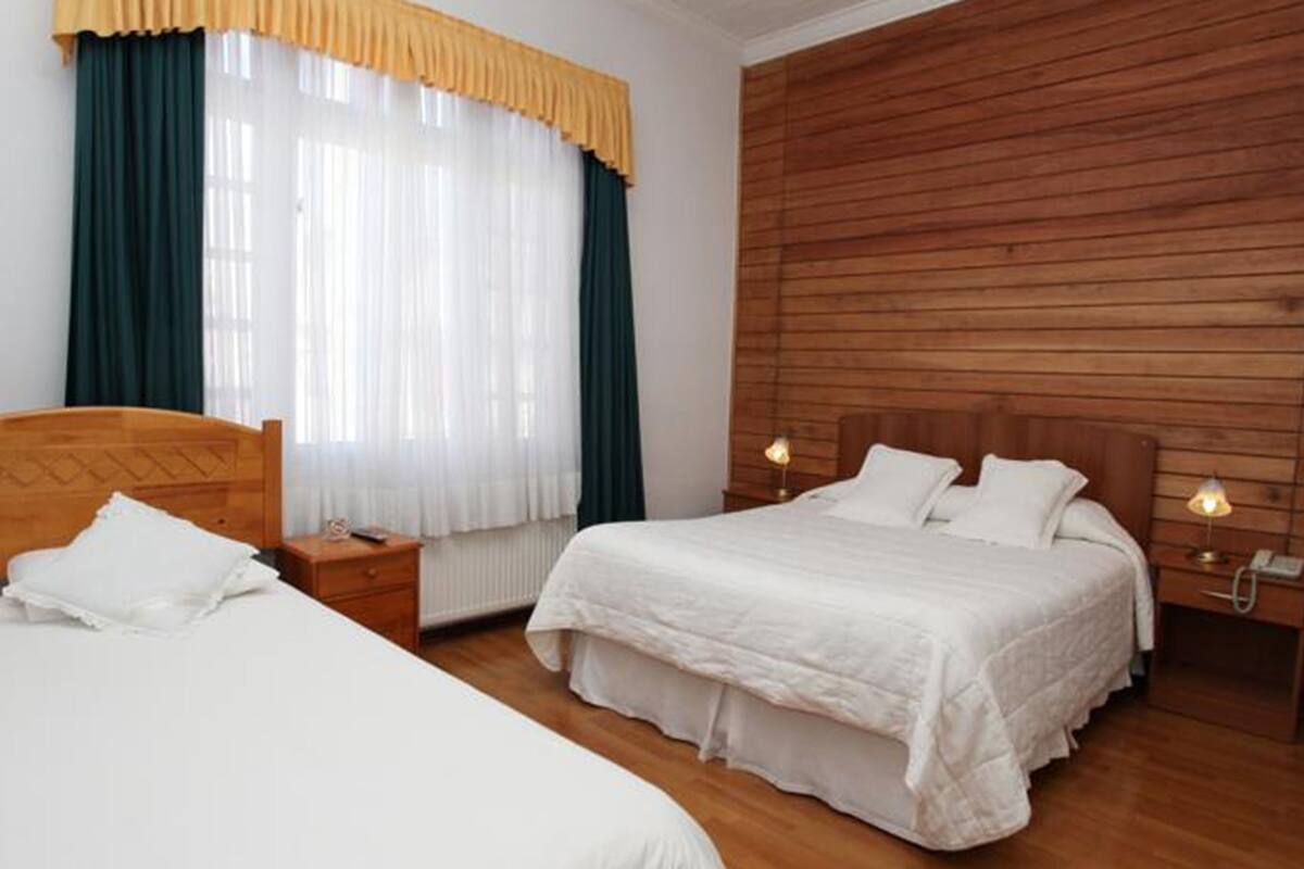 Ein Doppelzimmer mit zwei Betten, Holz-Kopfteilen, einer Holzwand, einem Fenster mit Vorhängen und Nachttischlampen.