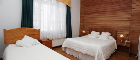 A double room with two beds, wooden headboards, a wooden wall, a window with curtains, and bedside lamps.