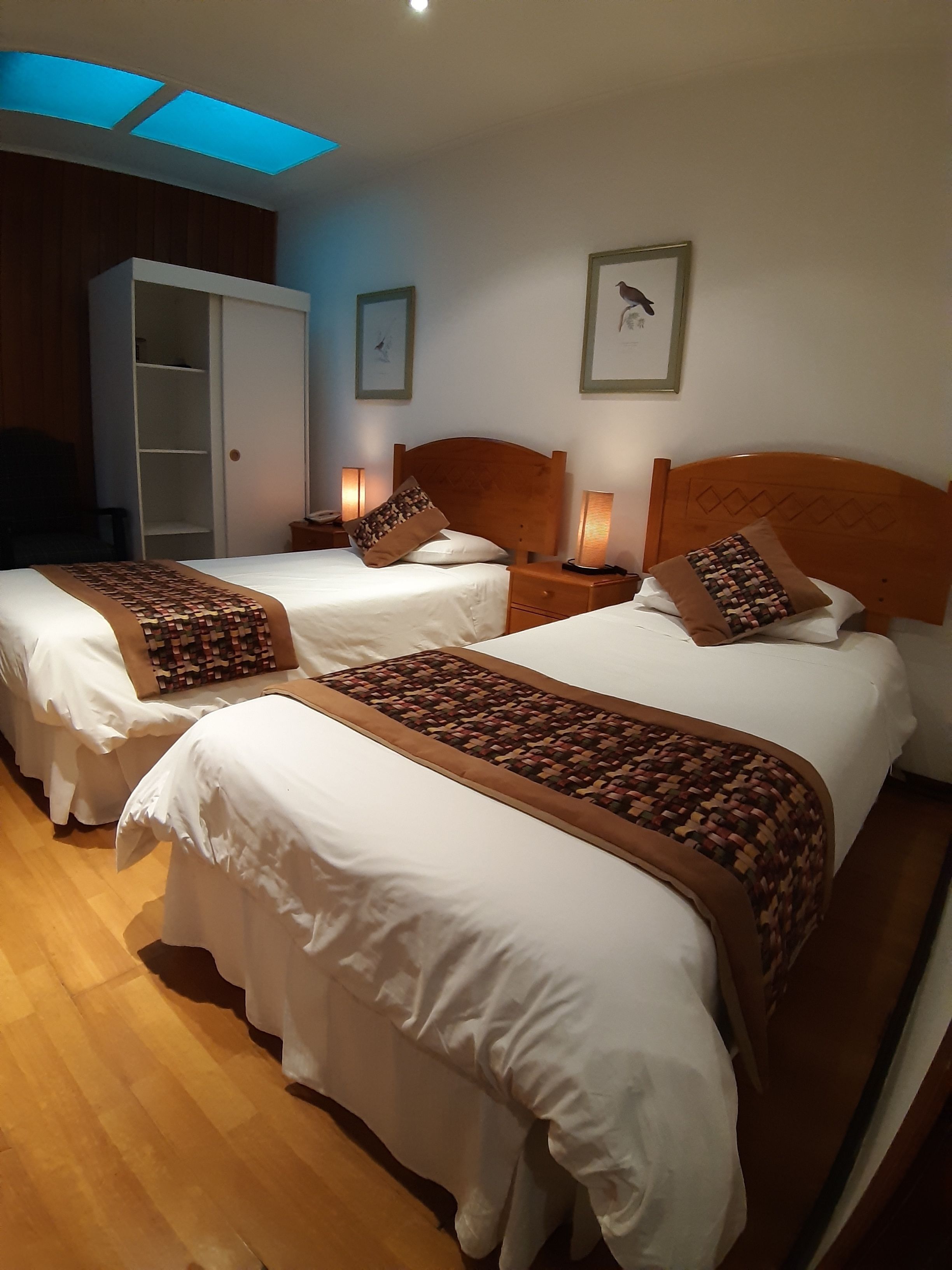 Habitación de hotel con dos camas, cabeceros de madera y lámparas de noche.