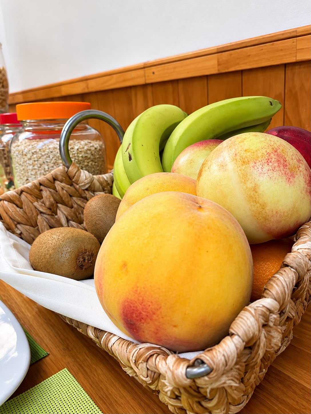 A wicker basket containing peaches, bananas, kiwi, and a jar of oats.