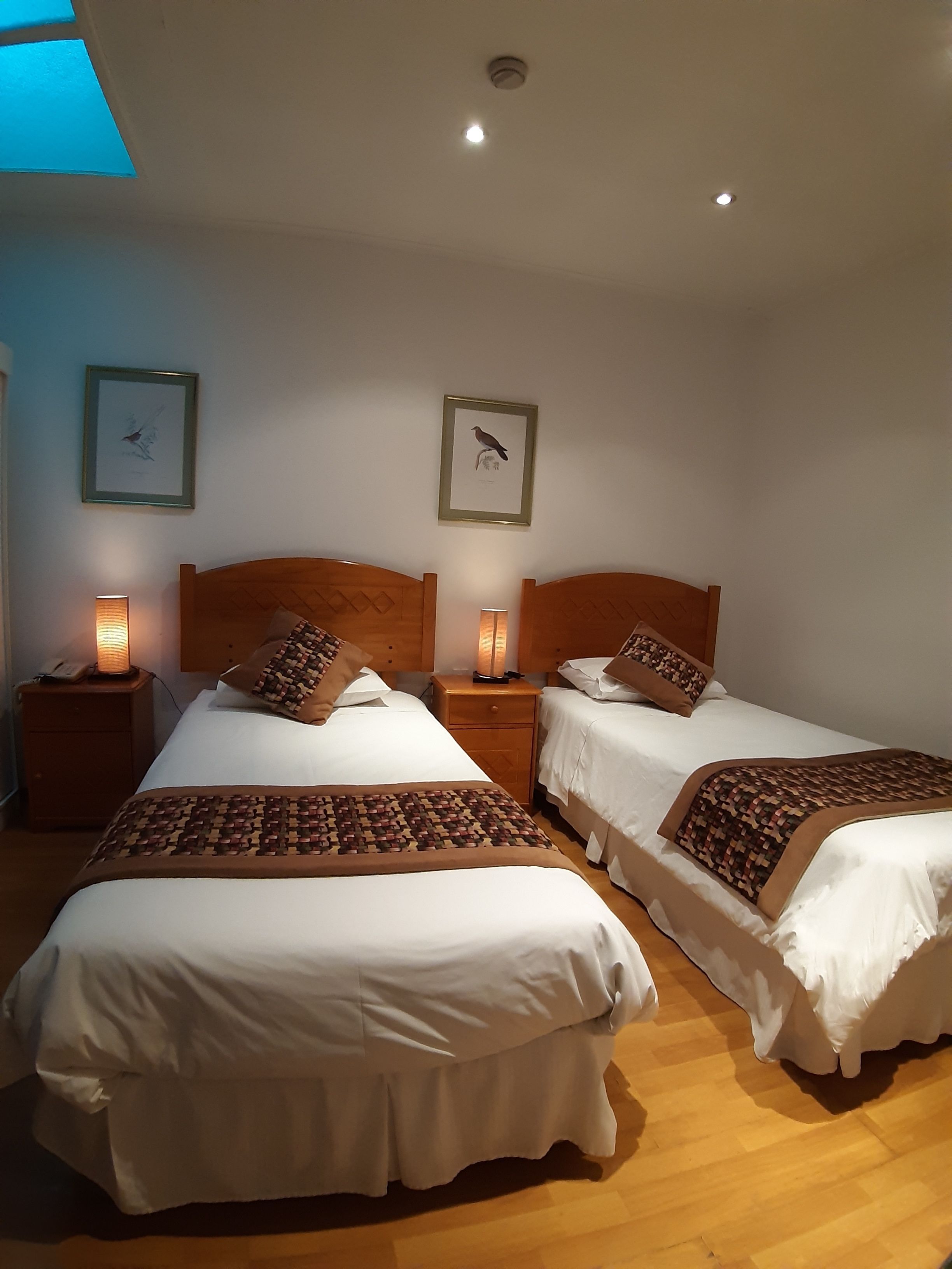 Habitación de hotel con dos camas, cabeceros de madera, ropa de cama blanca y cuadros en la pared.