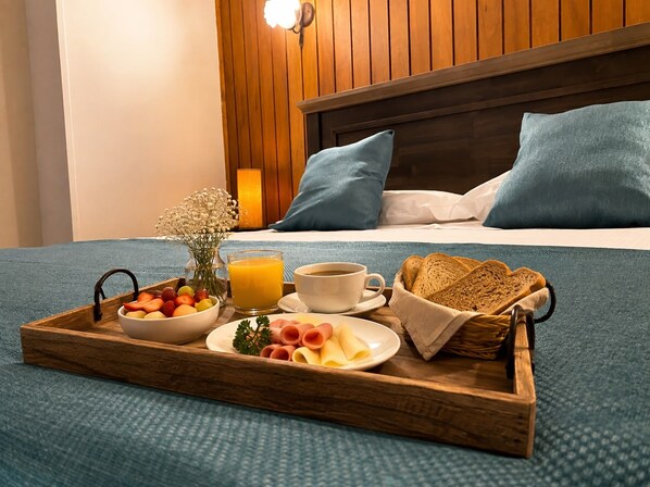 Una bandeja de desayuno bien dispuesta con frutas, pan y bebidas sobre una cama con almohadas azules y cabecera de madera.