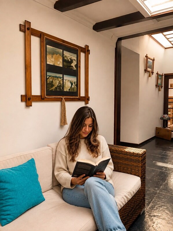 A person sitting on a sofa reading a book in a room with a framed artwork on the wall and a mirror reflecting the room. - Hostal de La Patagonia (Punta Arenas)