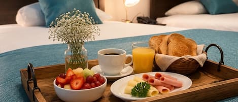 A breakfast tray on a bed with a cup of coffee, orange juice, bread, and a bowl of fruit.