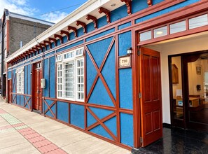 A building with a blue facade, a wooden door, and a window with white framing. - Hostal de La Patagonia (Punta Arenas)