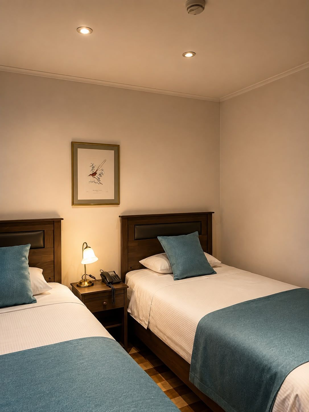 Ein Hotelzimmer mit zwei Betten, einem Nachttisch mit Lampe, einem gerahmten Bild an der Wand und einer Deckenleuchte.