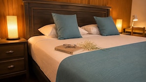 A neatly made bed with a blue blanket, two pillows, a bedside table with a lamp, and a book with glasses on it. - Hostal de La Patagonia (Punta Arenas)