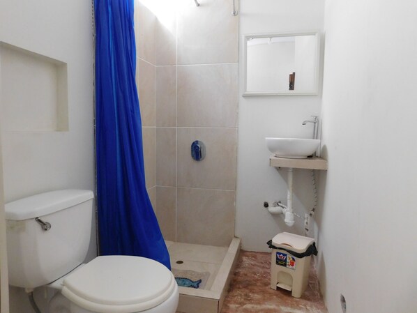 A small bathroom with a toilet, a sink, a shower, and a mirror. - Nuna Chak Hostel & Café (Víctor Larco Herrera)