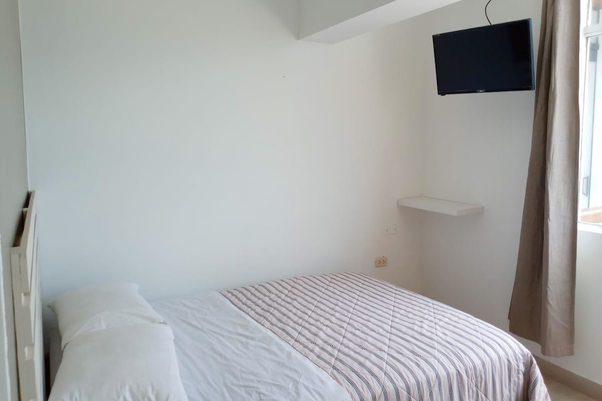 A bedroom with a bed, a mounted TV, and a window with curtains.