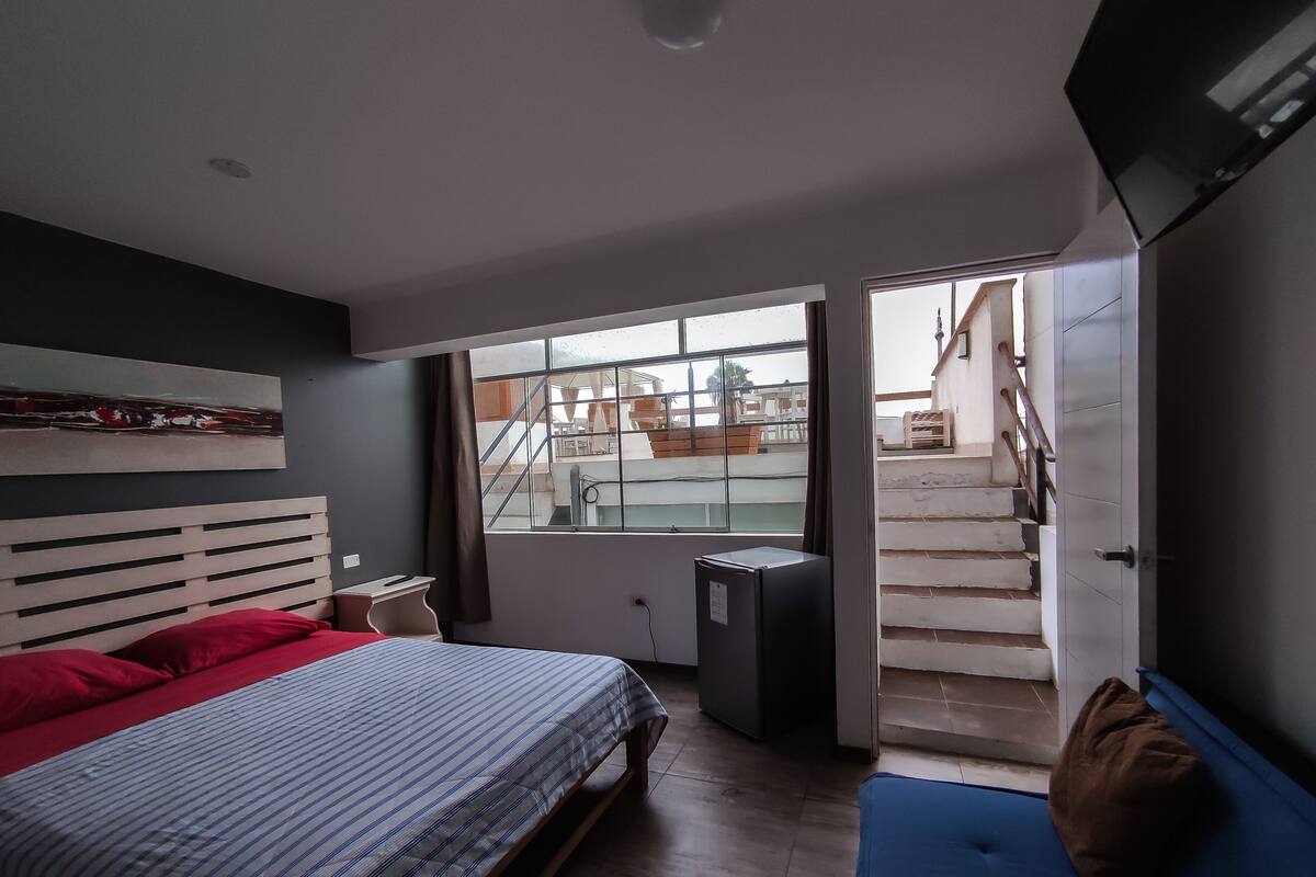 A bedroom with a bed, a window, a door, and a view of a staircase.