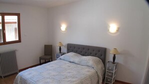 Un dormitorio con una cama, dos mesitas de noche con lámparas, una silla y un radiador.