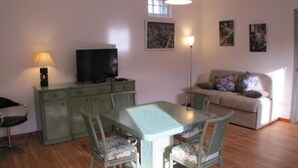 Una sala de estar con una mesa de comedor, sillas, un sofá, un televisor y obras de arte en las paredes.
