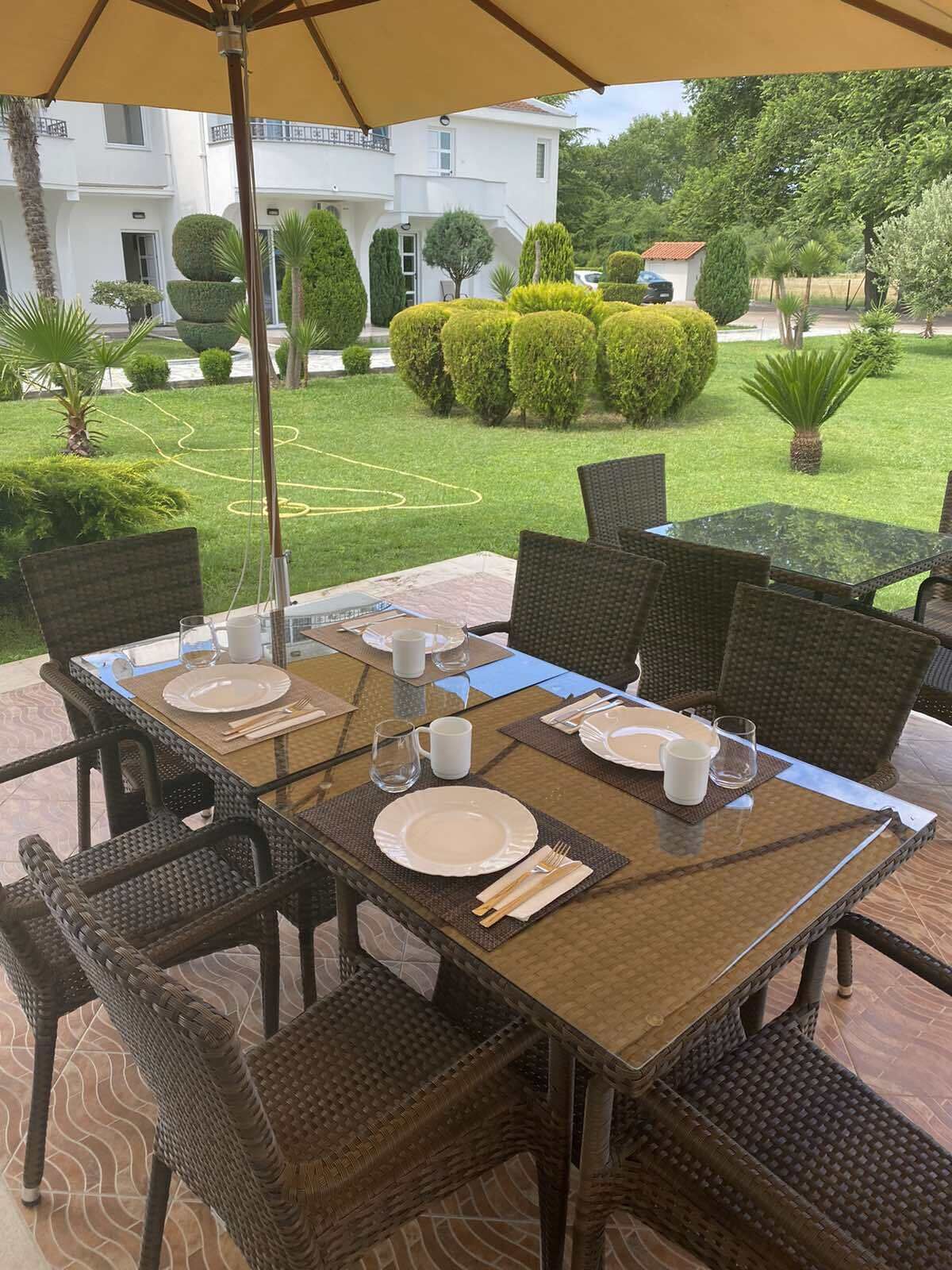 An outdoor dining area with a table set for four, surrounded by wicker chairs, under a large umbrella.