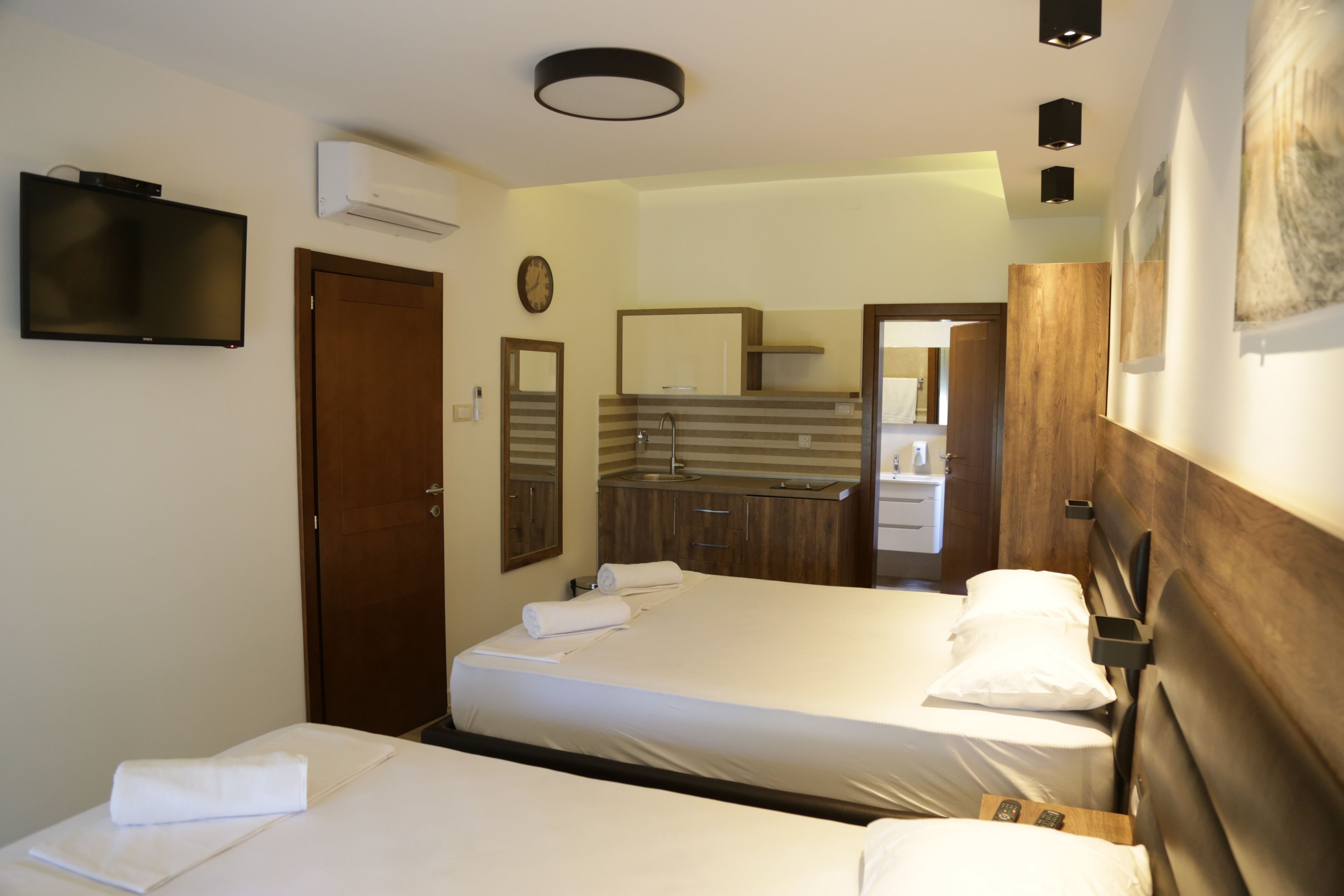 A hotel room with two beds, a TV, a mirror, and a bathroom visible through an open door.
