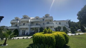 Un edificio de varios pisos con balcones, rodeado de céspedes cuidados y árboles.