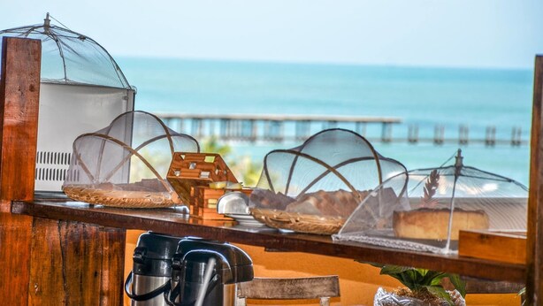 Un espace de restauration situé au bord de la plage, offrant une vue sur l’océan et une jetée en arrière-plan.