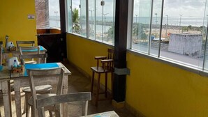 Un espace repas avec des tables et des chaises, une vue sur la plage et un panneau indiquant la zone surveillée par des sauveteurs.