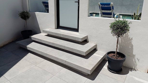 A modern outdoor area with a glass door, steps leading to a balcony, and potted plants.